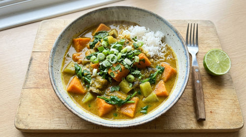 Caribbean sweet potato curry with aubergine and spinach in a golden coconut colombo sauce, seen from above in a wide bowl on a wooden board